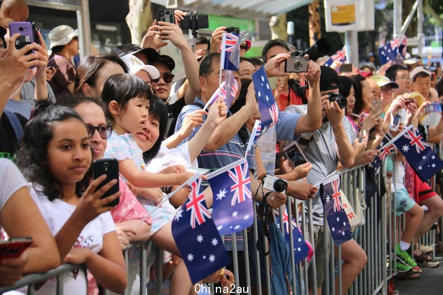 A crowd of people wave flags and take photos at Melbourne's Australia Day parade