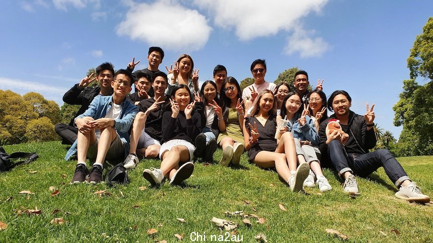 A large group of young Asian people sitting on a green hill on a sunny day