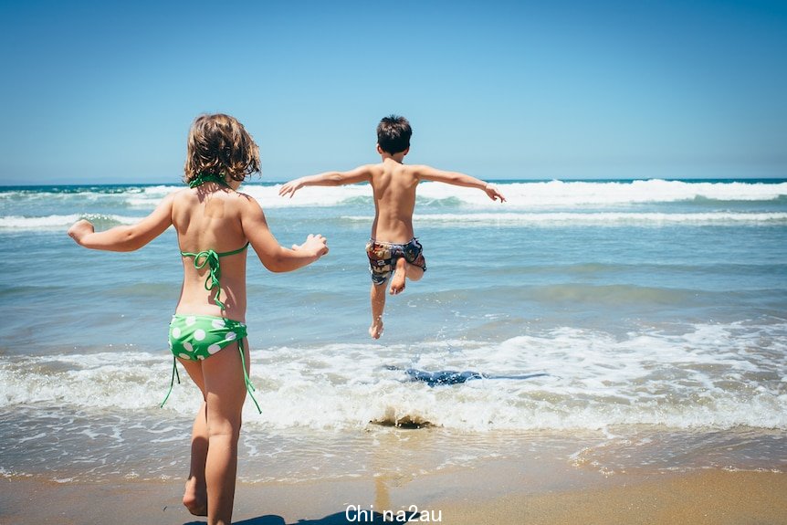 Two kids leap into the surf on a sunny day.