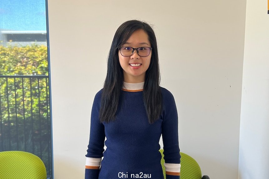 Image of Irene Teo standing in navy sweater, black pants with long black hair and glasses, infront of office chairs, glass door