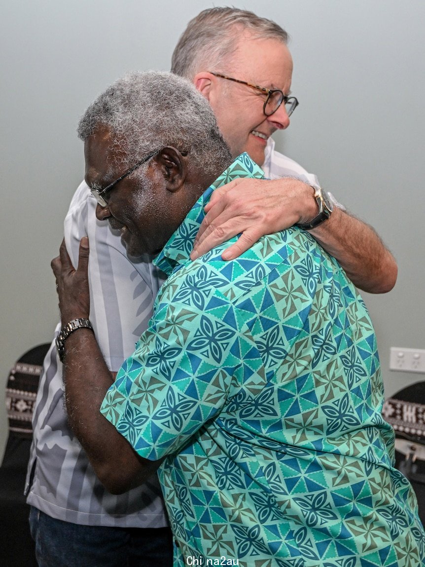 Two men embrace wearing colourful Pacific print shirts