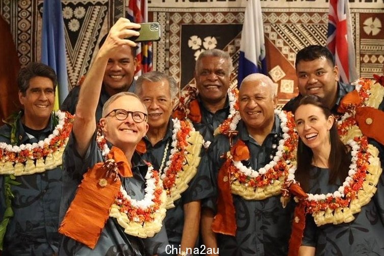 Anthony Albanese holds a phone as members of the Pacific Island Forum, all wearing traditional dress, pose for a group selfie