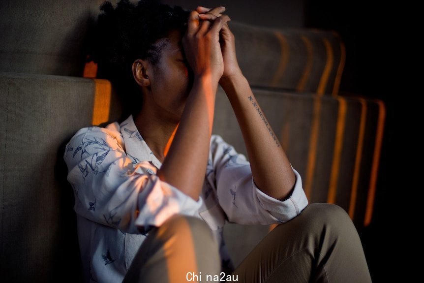 Woman sits down with hands clasped over her face.