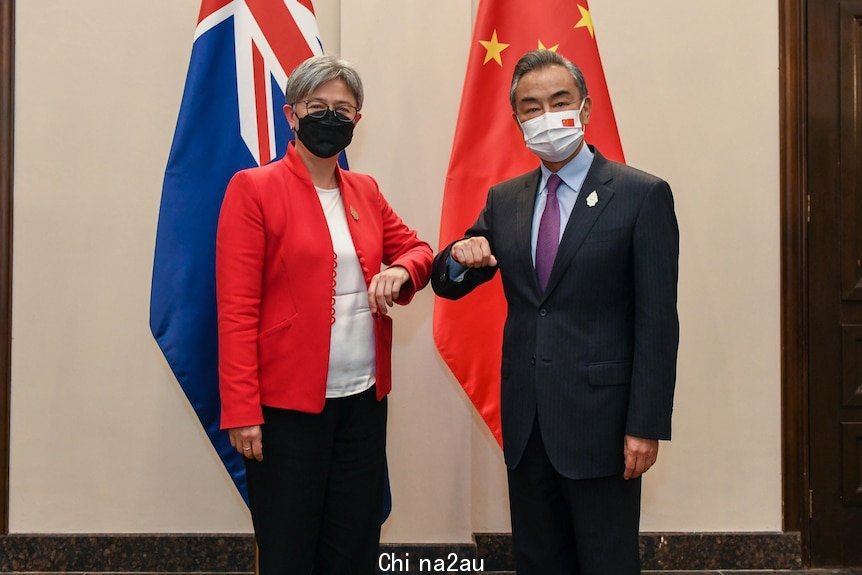 A man and woman bump elbows for the camera with the Australian and Chinese flags behind them.