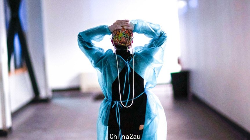 A woman in scrubs walking down a hallway with her hands on her head