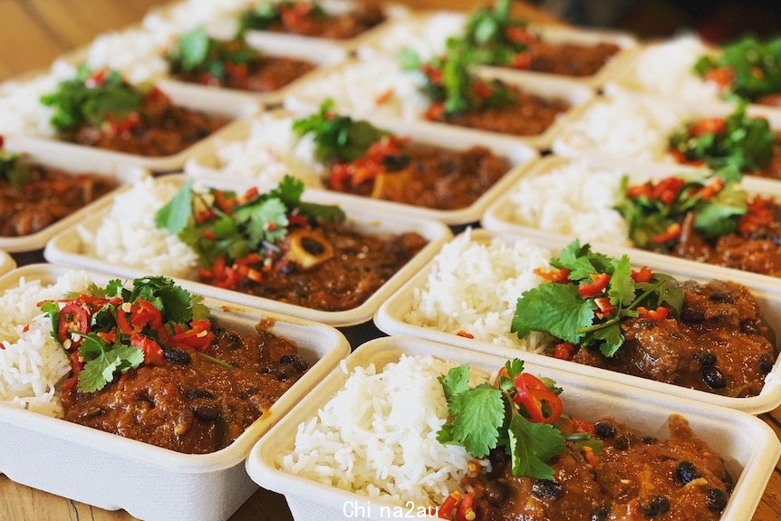 Containers with goat curry and rice lined up on a benchtop