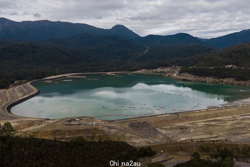 A large dam holding light-blue water surrounded by forest.