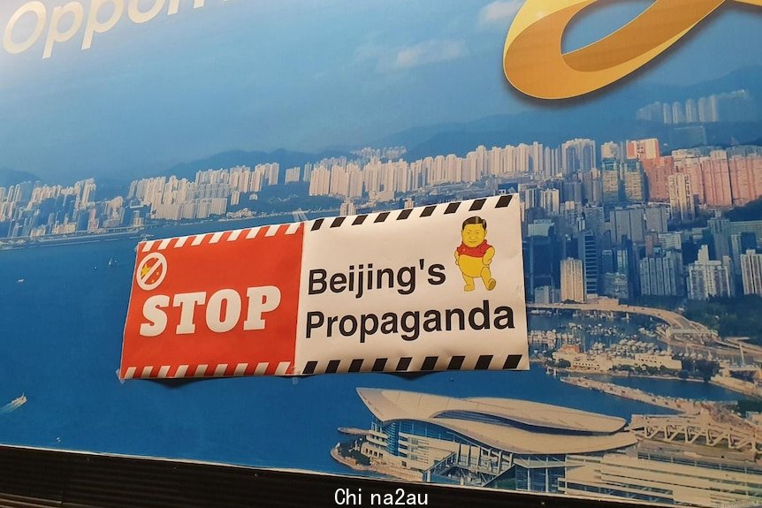 A black, white and red sign with the words Stop Beijing propaganda was placed over a billboard of Hong Kong
