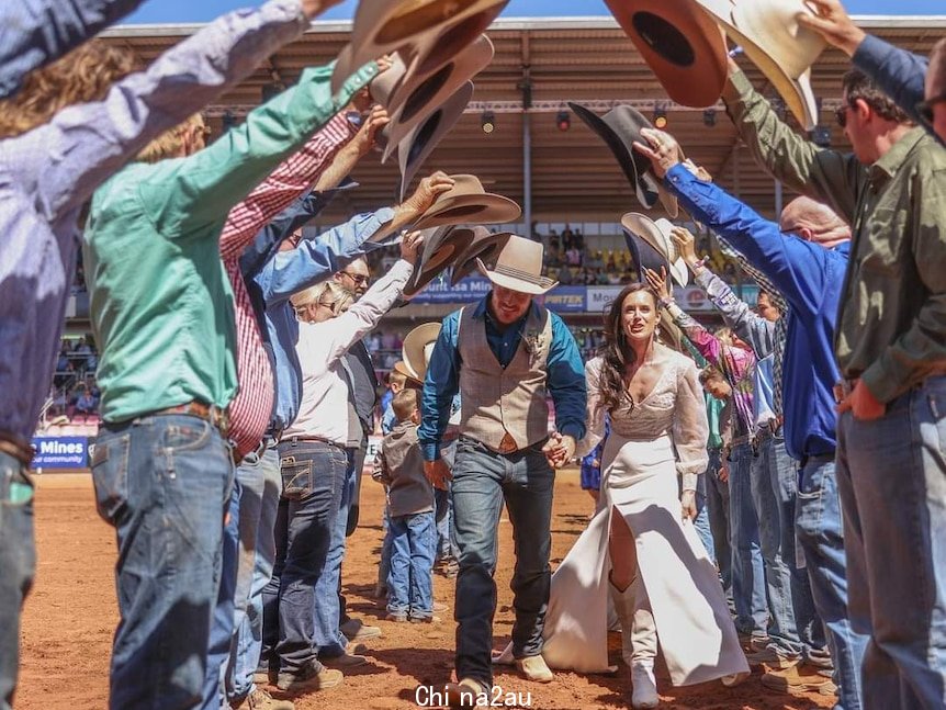 newlywed couple walks through cowboy guard of honour on rodeo arena