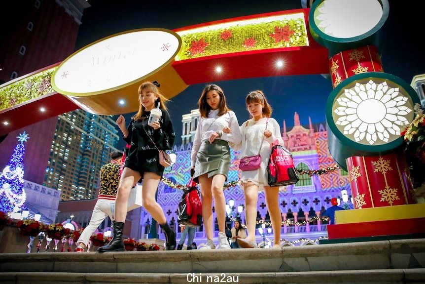 Three young women walk down a set of stairs surrounded by fluorescent lights in Macau