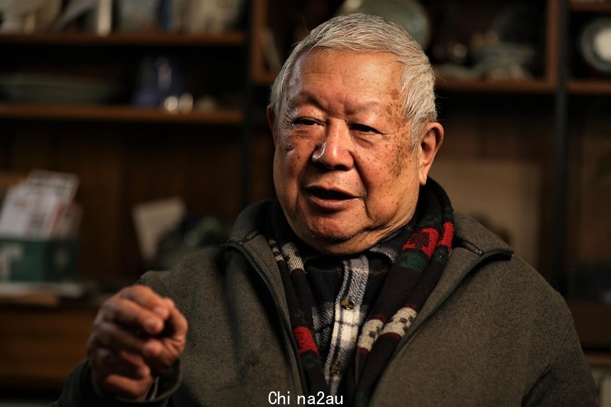 A man with short grey hair sits in a warm lit room during an interview