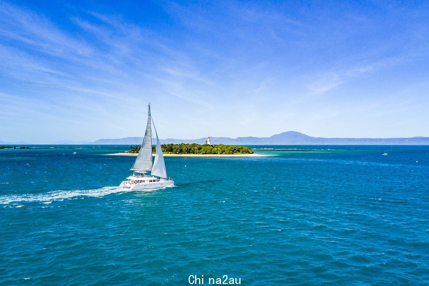 A sailing boat approaches an island.
