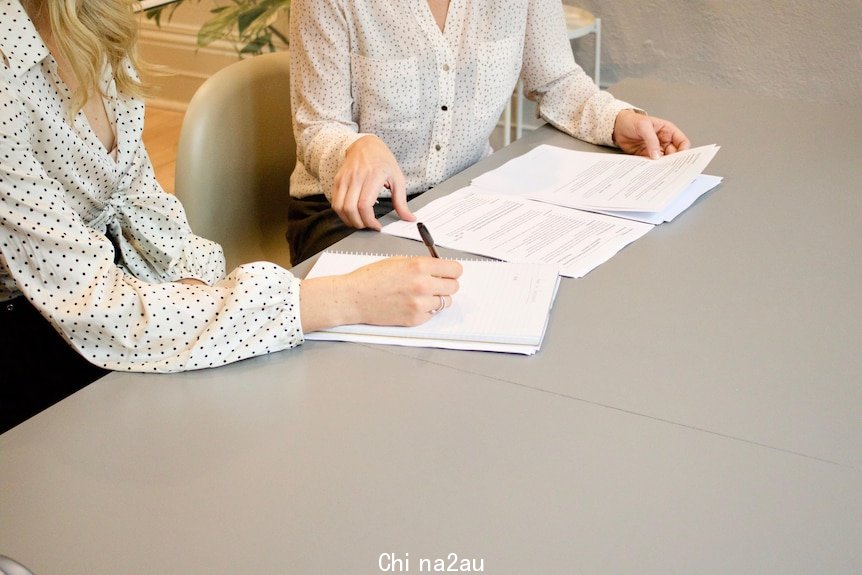 Two women in white button-down shirts look over papers