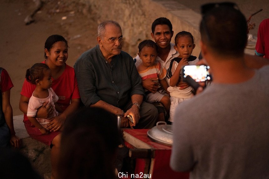 Two men and a woman sit with three small children while someone take a photo of them.