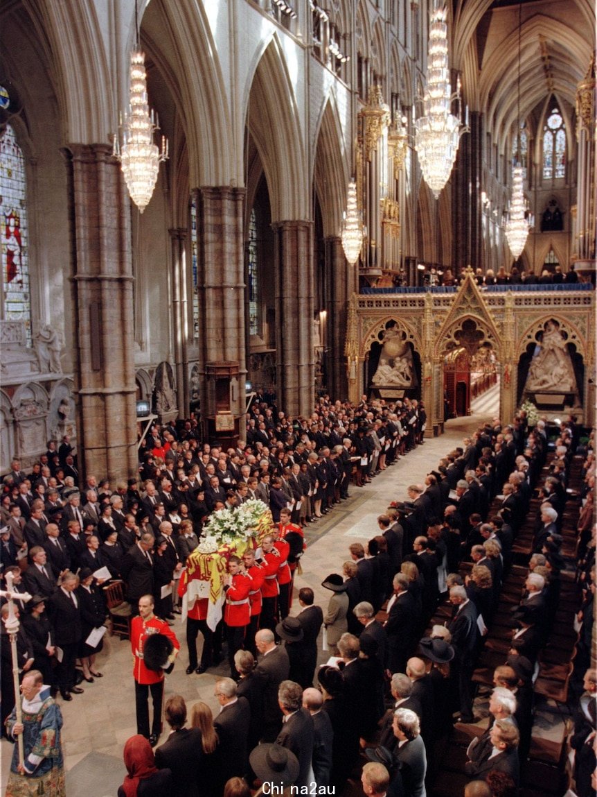 A coffin is carried by uniformed pall bearers down the aisle of the huge cathetral-like building.