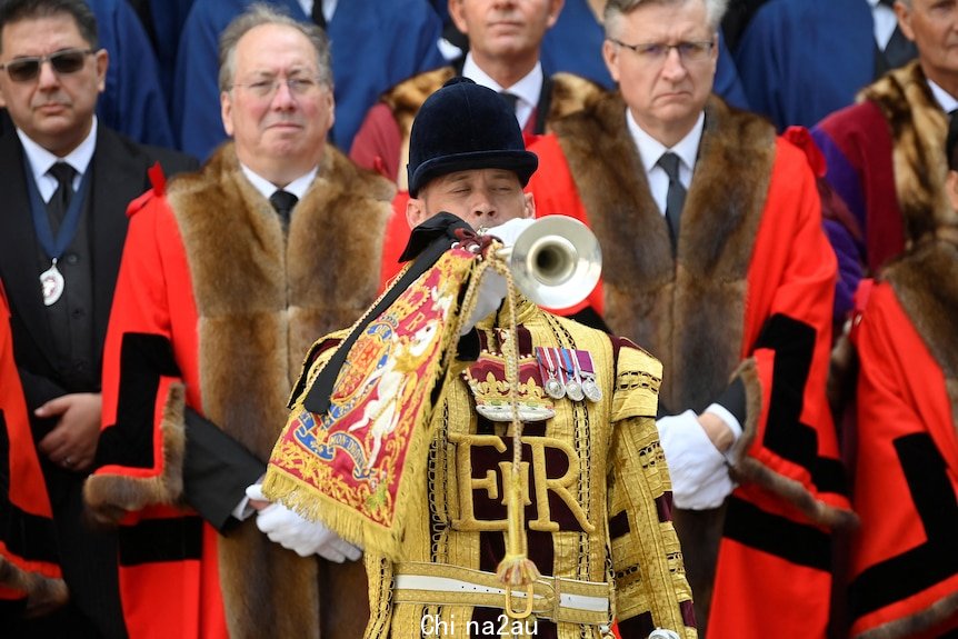 A trumpeter dressed in gold plays in front of men in red and fur robes. 