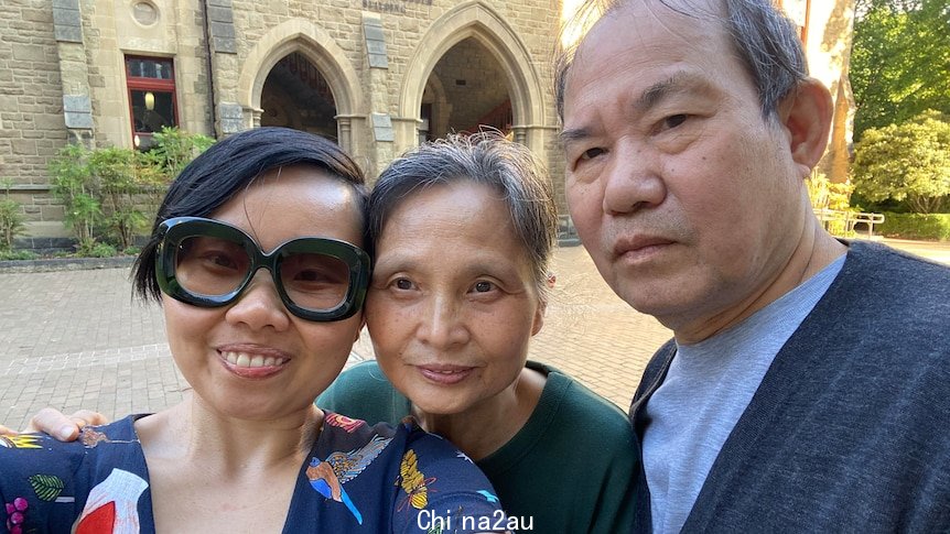 Grace Feng Fang Juan smiles as she poses for a selfie with her parents in front of an old stone building