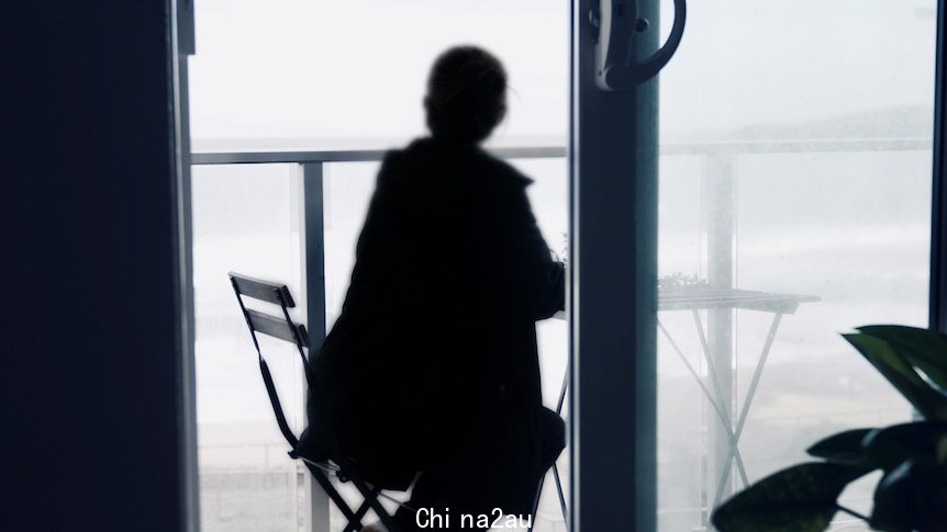 Woman sitting on a balcony, facing away to the ocean.