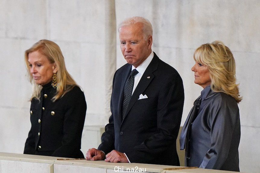 Joe stands on a balcony with a somber expression.