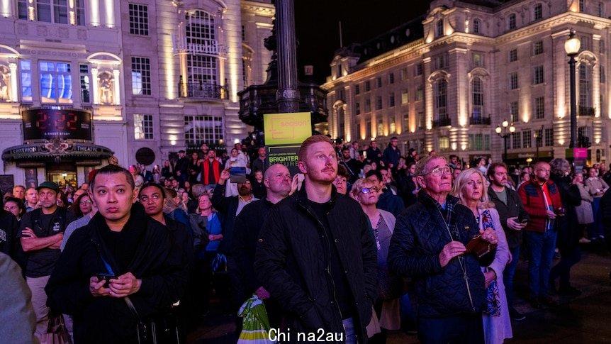 A crowd of people stand together on a dark English street.