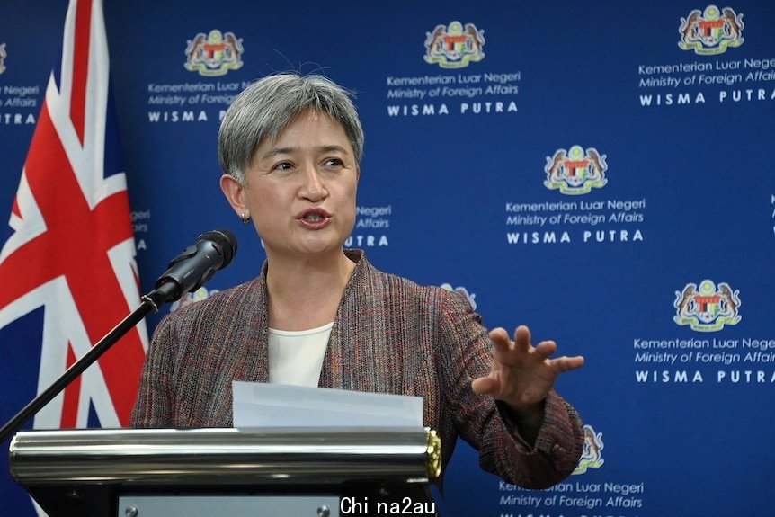 Penny Wong speaking at a microphone in front of a blue background in a press conference in Malaysia