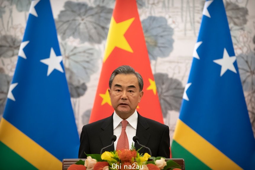 Wang Yi stands at a lectern in front of an Chinese and two Solomon Islands flags. 