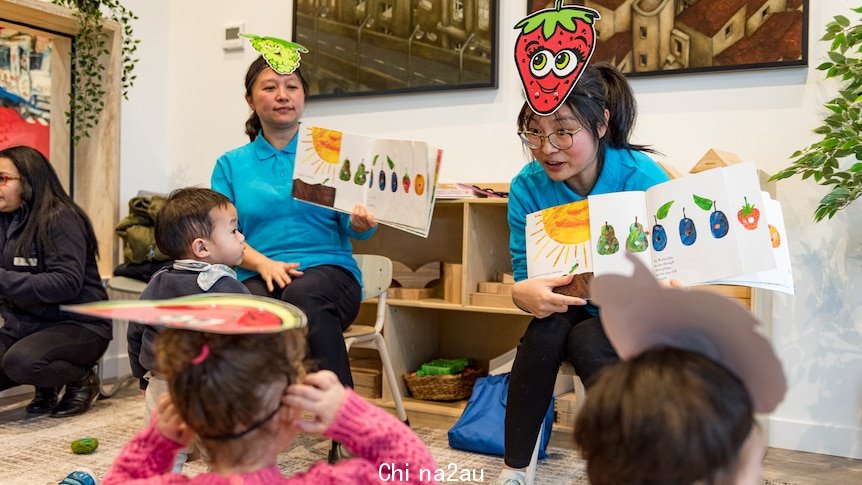 Photo of two women wearing colourful hats and holding books speaking in an animated way with children 