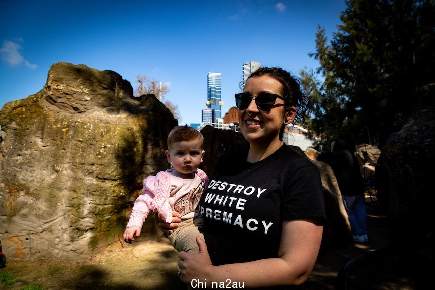 A person with a baby in front of the Melbourne skyline.