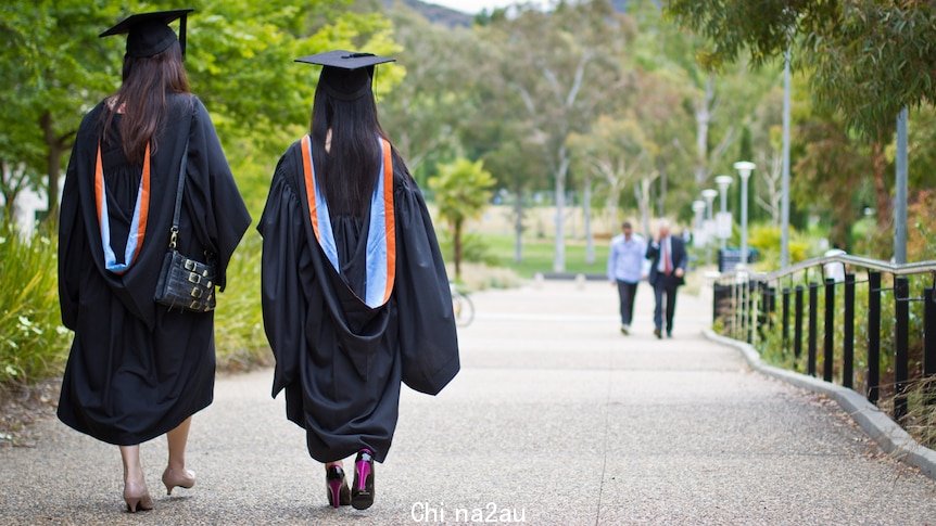 Two women walk through university grounds in graduation robes