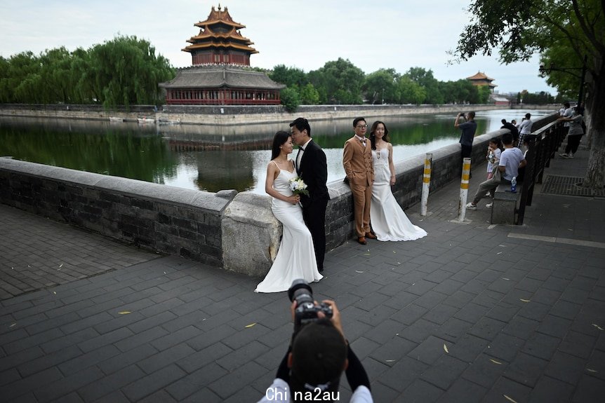 Two couples in wedding outfits post for photos in front of a canal.