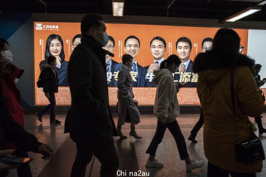 Chinese commuters walk past a billboard in a subway