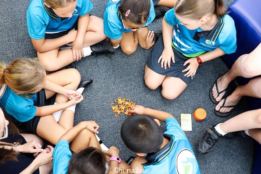 New prep-aged children sit on floor in circle in prep classroom playing barrel of monkeys game.