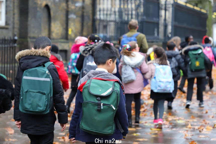 Primary school kids carrying backpacks on a rainy winter day.