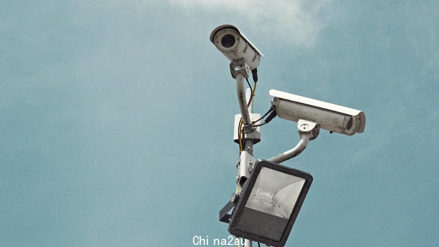 Two security cameras against a grey sky.