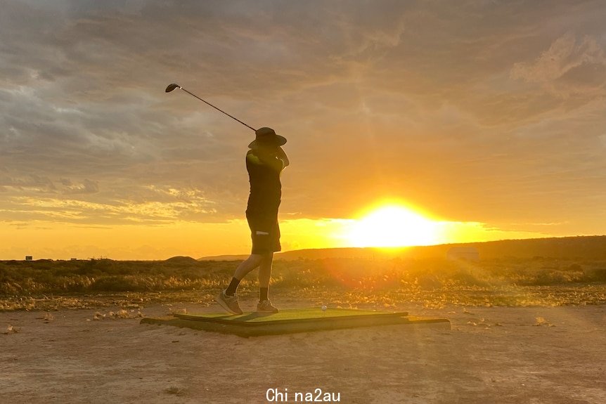 Golfer hitting a ball in front of a setting sun.