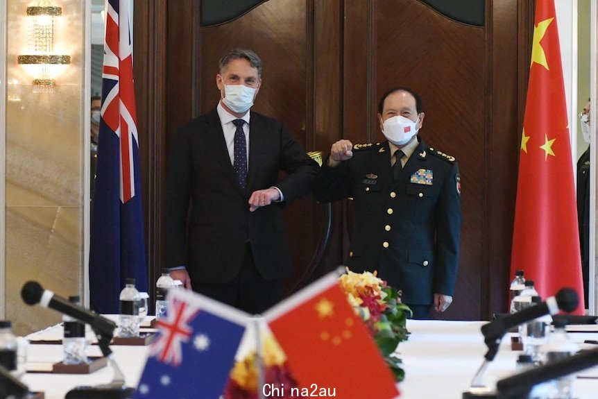 Richard Marles and Wei Fenghe bump elbows as they wear masks and stand near their countries flags
