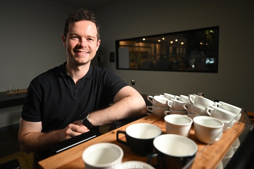 barista anthony douglas smiles and leans on a coffee machine with coffee cups stacked on it