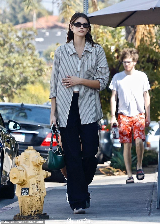 Fashionable: Gerber 在一件白色衬衫上穿了一件条纹纽扣衬衫,露出了她的腹部的一小部分
