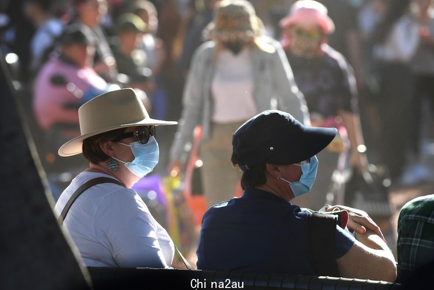 two people sitting watching outdoor entertainment wearing blue surgical masks