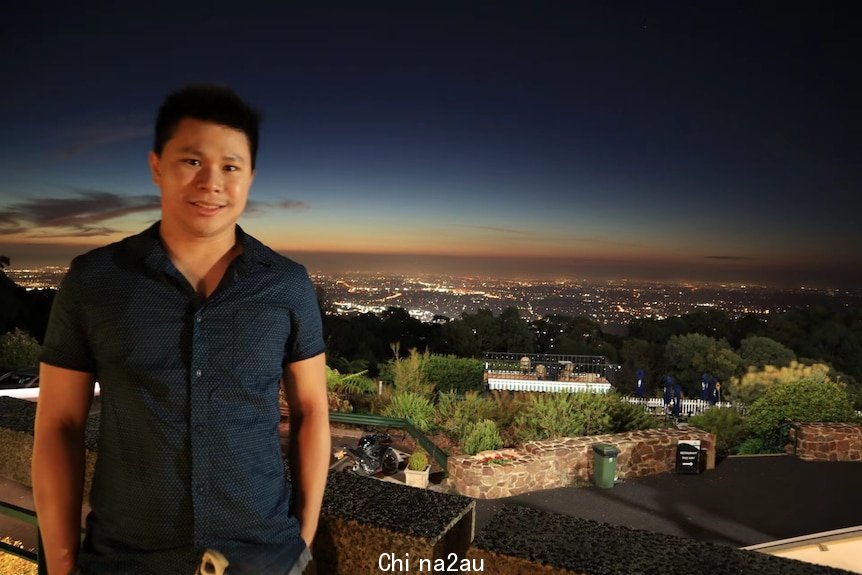 一名亚洲男子站在阳台生背后是夜景