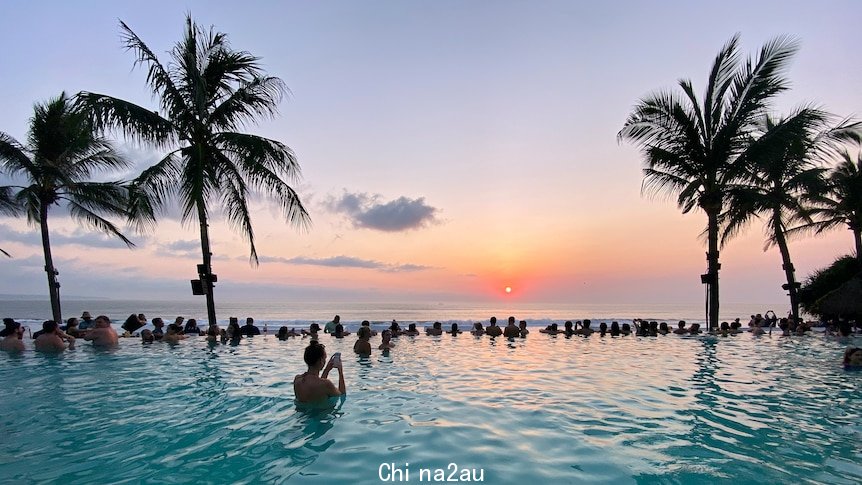 People swimming in a pool facing the ocean during sunset in Seminyak Beach, Bali, Indonesia.