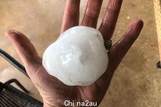A woman holds a hail stone the size of a cricket ball in her hands. 