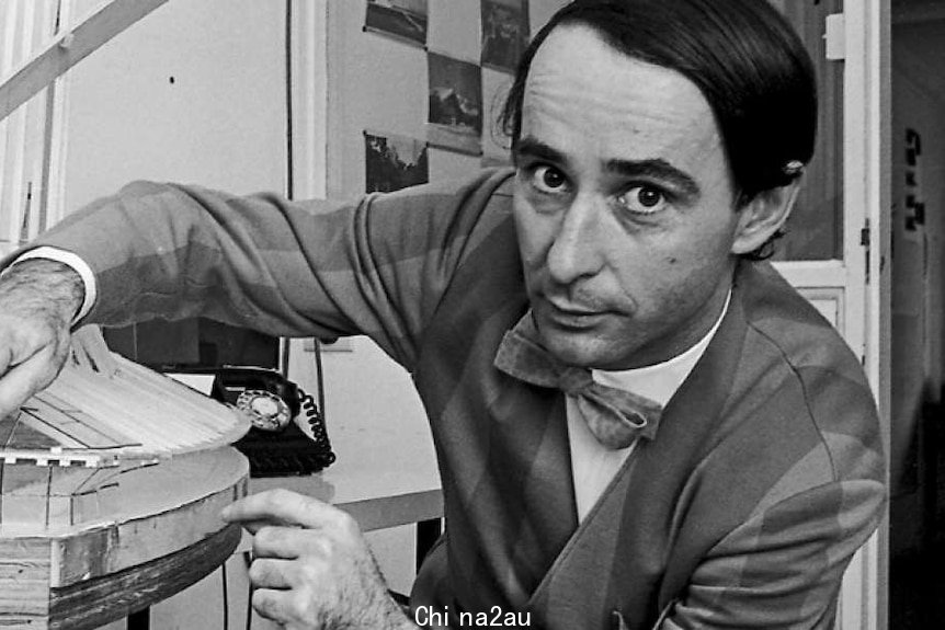 Black and white photo of a white man with dark hair in a striped suit and bow-tie beside a glass model of the Opera House.