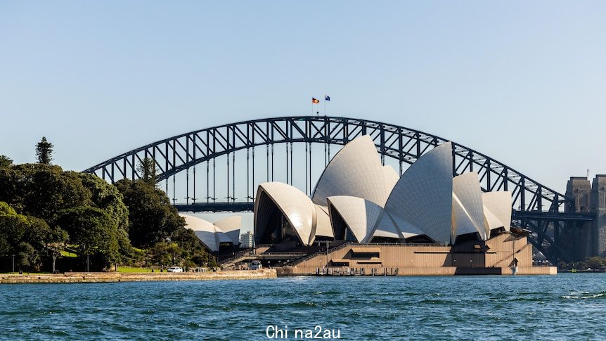 White tiled sails of the Sydney Opera House peak up into a clear blue sky with the Sydney Harbour Bridge in the background.