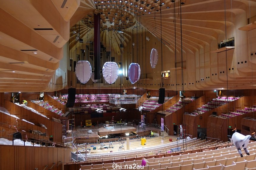 The inside of a large and grand concert hall under construction - four large reflector panels are suspended from the ceiling.