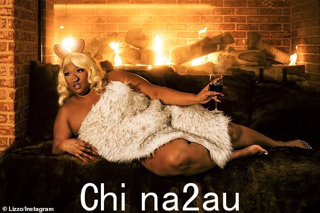 所以过来吧:Lizzo 还戴着金色假发,在火炉边赤身裸体,手里拿着一杯酒;她身上只有一个假毛皮扔