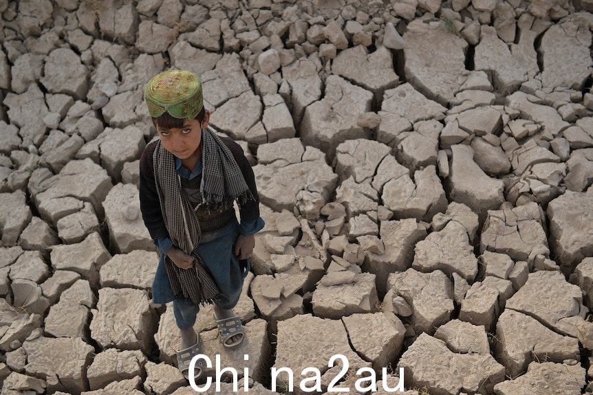 A child stands on dry cracked land.