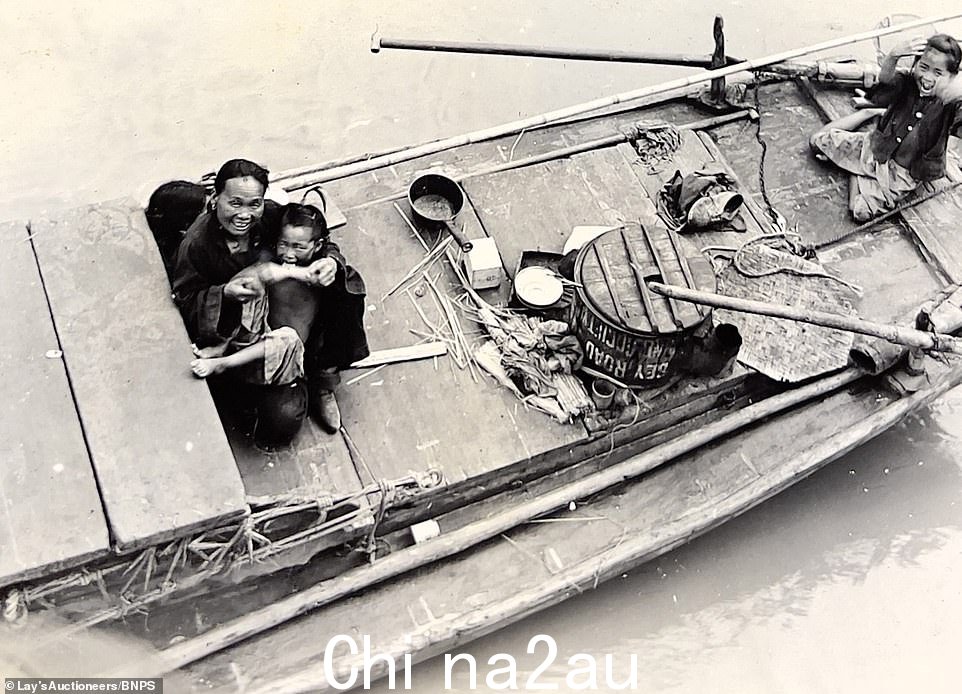 看到一个微笑的中国母亲抱着她的孩子在船上，而另一个年轻人抬头看着摄影师微笑