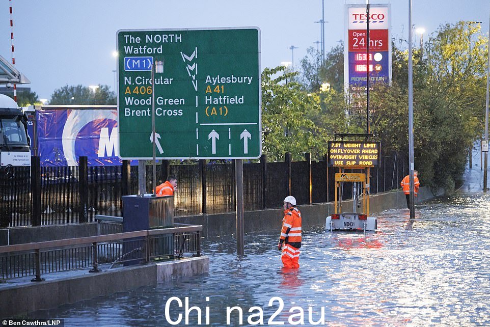 一名工人站在伦敦北部 A41 Hendon Way 的洪水中,暴雨过后该路现已完全关闭