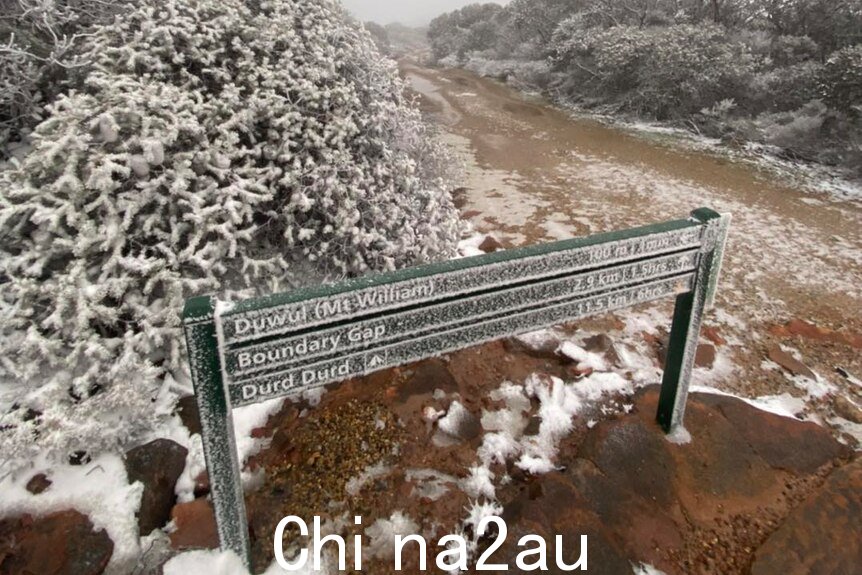 A sign at the foot of an alpine trail dusted with snow.